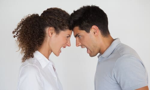 A man and a woman, each in light, collared shirts, yelling at each other while butting heads.