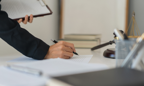A medicaid trust lawyer signing documents while holding a clipboard behind a desk.